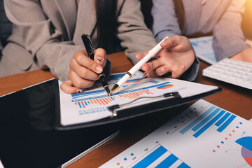 Group of confident business people point to graphs and charts to analyze market data, balance sheet, account, net profit to plan new sales strategies to increase production capacity.