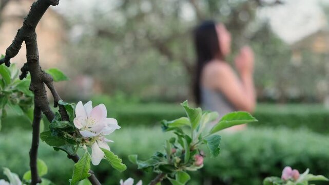 Woman Sneezes While Walking in the Park. Seasonal Allergies Affecting Outdoor Activities. Spring Allergy Symptoms. Reaction to Pollen. Blurred Background in the Foreground Flowering Branch With Flower