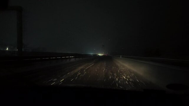 POV winter driving in snowstorm at night. Dangerous foggy and icy road. Front car windshield with moving wipers and beams of car headlights. Winter on a Hungarian motorway.