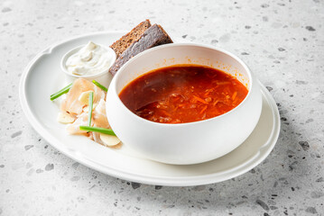 A comforting bowl of soup served with dark bread, sour cream, and fresh herbs on a stylish white plate, ideal for showcasing warm, hearty meals and traditional cuisine.
