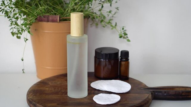Natural homemade face toner in frosted glass bottle with essential oil and face cream in amber glass jar. Set on dark wood and marble background. Organic skincare and beauty concept.