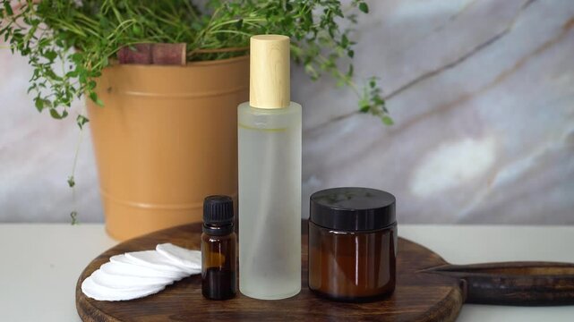 Natural homemade face toner in frosted glass bottle with essential oil and face cream in amber glass jar. Set on dark wood and marble background. Organic skincare and beauty concept.