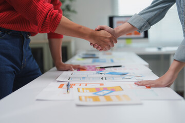 Two web designers shaking hands after a successful meeting about a new mobile application, celebrating the agreement over the design and development of the user interface