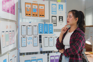 Uxui designer examines mobile app prototypes on a wall, focusing on layout and functionality. The...
