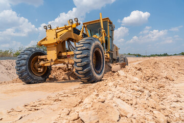 A robust yellow motor grader works tirelessly on a vast construction site, its blade carving...