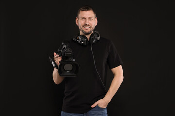 Fototapeta premium Man with professional video camera and headset on black background