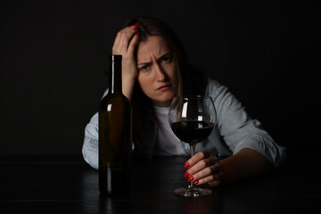 Alcohol addiction. Miserable woman with wine at table in dark