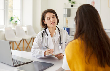 Fototapeta premium Female young woman patient visiting friendly doctor sitting at the desk in office on her workplace and having consultation during medical examination in clinic. Medicine and health care concept.