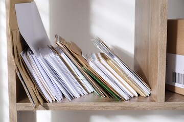 Different paper envelopes on wooden shelf in post office, closeup