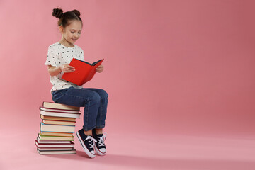 Cute girl reading book on pink background, space for text