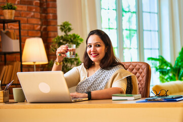 Hydrating after health reminder, Indian woman in saree drinks water during office work