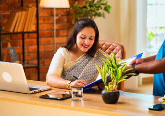 Indian woman in saree signs file while working on laptop at cozy corporate desk