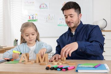 Little girl learning letters with teacher at desk indoors