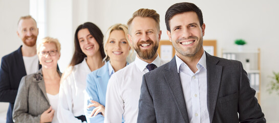 Cheerful team of business professionals standing together in line in bright office space and looking confidently at camera. Group portrait of successful smiling colleagues in positive work environment