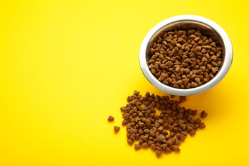 Dog or cat dry food in a silver bowl on yellow background. Space for text