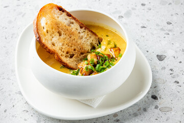 A comforting bowl of creamy soup topped with sautéed vegetables and herbs, accompanied by a slice of toasted bread, elegantly presented on a white plate, ideal for showcasing hearty meals.