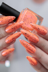 Woman hand with long nails and light orange neon manicure