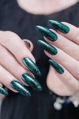Woman's hand with long nails and black green nail polish
