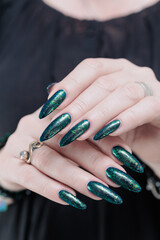 Woman's hand with long nails and black green nail polish
