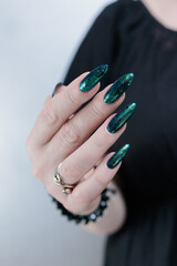 Woman's hand with long nails and black green nail polish