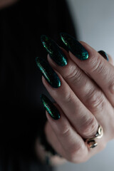 Woman's hand with long nails and black green nail polish