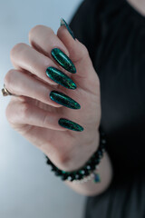 Woman's hand with long nails and black green nail polish