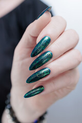 Woman's hand with long nails and black green nail polish
