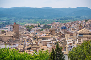 A panoramic view of the historic town of Segorbe, Castell&oacute;n Province, Spain, with tiled rooftops, church towers, and surrounding countryside under a bright summer sky