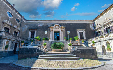 CATANIA, ITALY. Ornate baroque courtyard and stone staircase of the historic Palazzo Biscari, featuring classical sculptures and architectural details under a blue sky in Sicily.