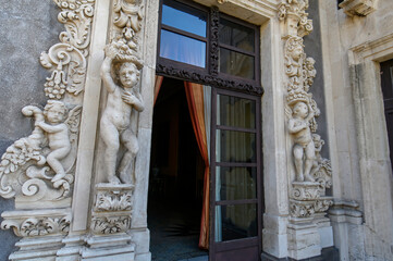 CATANIA, ITALY. Ornate baroque courtyard and stone staircase of the historic Palazzo Biscari, featuring classical sculptures and architectural details under a blue sky in Sicily.