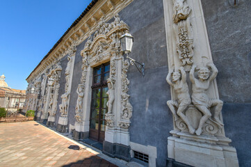 CATANIA, ITALY. Ornate baroque courtyard and stone staircase of the historic Palazzo Biscari, featuring classical sculptures and architectural details under a blue sky in Sicily.