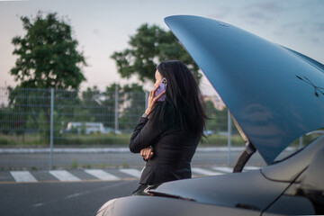 Young woman calling insurance after car breakdown outdoors, open hood. Back view. Waiting for help....