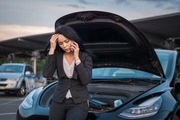 Upset young woman talking to insurance company after car breakdown, standing outdoors, open car...