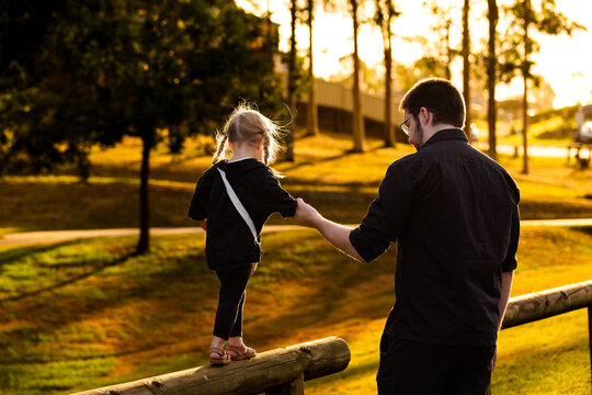 Child showing trust walking along post holding to fathers hand in golden light