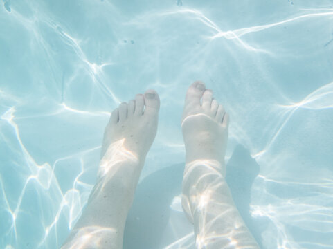 criss cross patterns of rippling light on feet underwater in pool