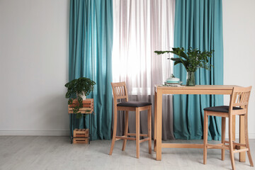 Stylish wooden table and chairs near window with elegant curtains in room