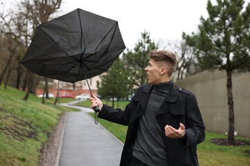 Man with broken umbrella fighting wind under rain outdoors