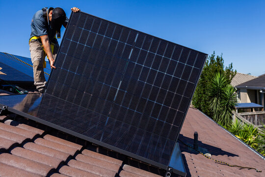 Aussie tradie apprentice helping install solar panels on hot sunlit roof of Australian home