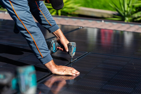 Electrician tradie man clamping down bifacial solar panels on roof during installation job