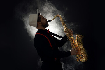 Naklejka premium Professional musician playing saxophone on black background with smoke