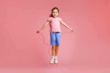 Cute little girl with jump rope on light pink background