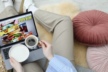 Blogger holding coffee near laptop with food blog web site on floor indoors, above view