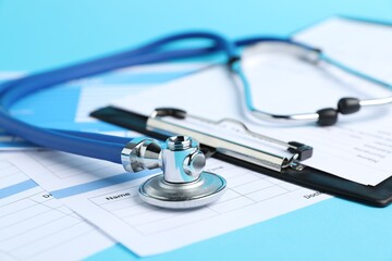 Stethoscope and medical card forms on light blue background, closeup