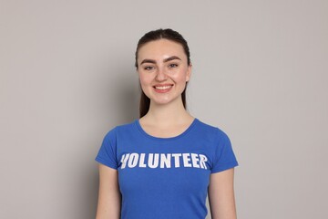 Portrait of smiling woman in t-shirt with word Volunteer on grey background