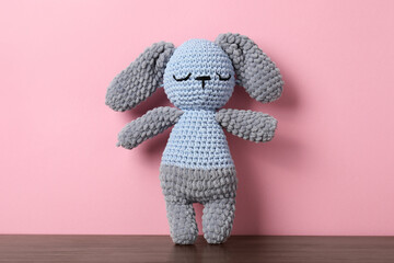 Cute knitted toy bunny on wooden table against pink background
