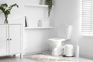 Toilet, brush and necessities near white wall in bathroom