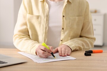 Woman highlighting important information at wooden desk indoors, closeup