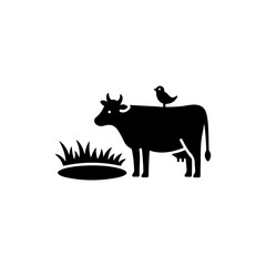 A Cow Standing Near a Pond with a Small Bird Perched on Its Back