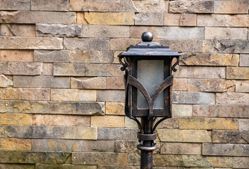 Antique-style black metal street lamp against natural stone wall.Vintage wrought iron lamp post against stone brick wall background.