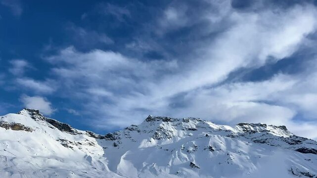 Time-lapse of snow-capped Swiss Alps and blue sky with fast-moving clouds. Natural background with mountain scenery. Winter landscape in the Engstligenalp, Adelboden region, Switzerland.